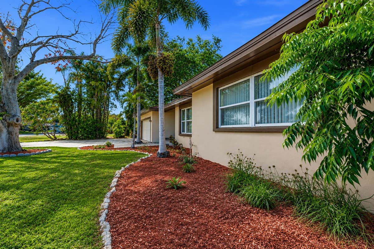 Side exterior view of the home surrounded by mature trees and tropical greenery.