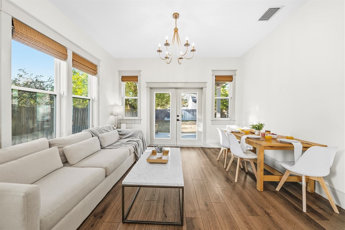 Elegant dining area with a gorgeous gold chandelier, bright white table and chairs, and floor-to-ceiling windows with warm wood blinds. The perfect setting for a memorable meal in this brand-new Seminole Heights home.