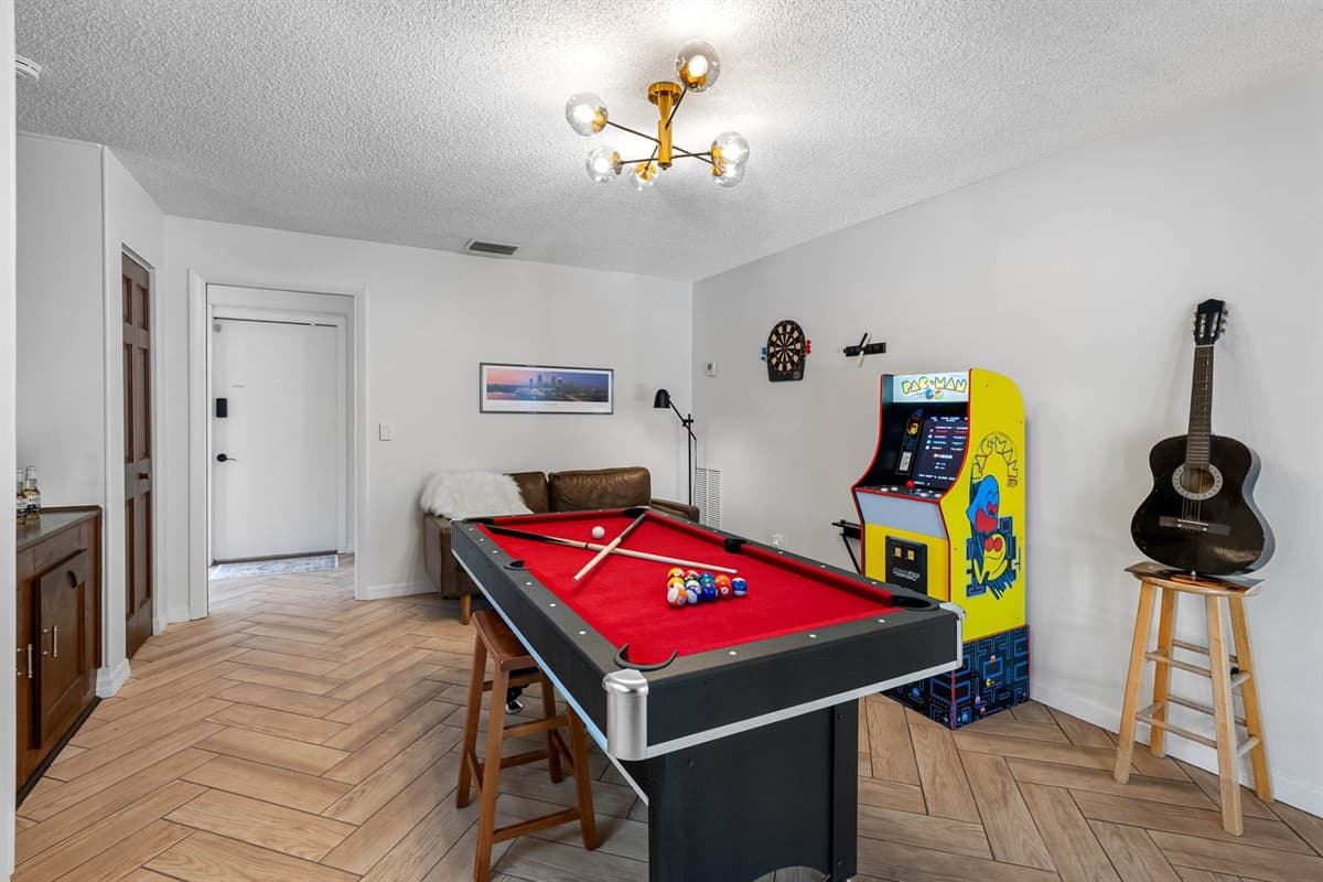 Retro vibes meet modern fun in this game room, featuring a full-size ping pong table, Pac-Man arcade machine, cozy lounge area, and stocked game shelf for endless entertainment.