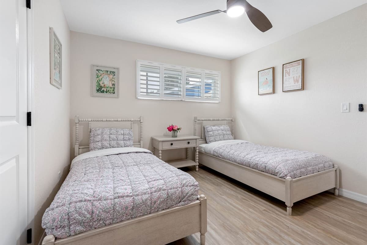 Neutral walls and wood-look flooring create a serene setting for two twin beds dressed in soft floral bedding, perfect for a beach getaway.