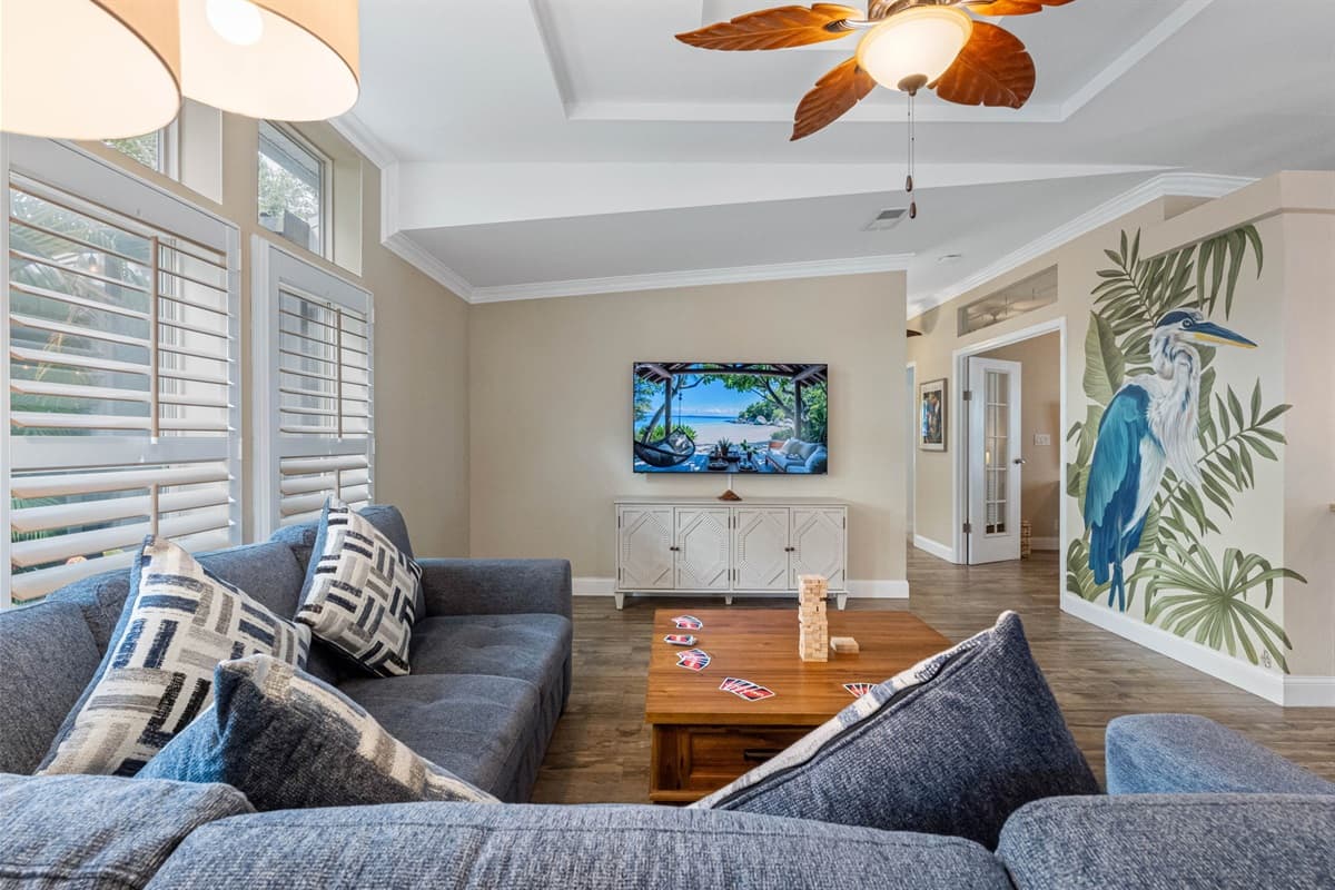 Step into a bright, inviting living room featuring a plush sectional sofa, tropical ceiling fans, and a large smart TV—perfect for family gatherings or cozy nights in.