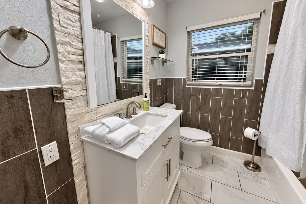 This freshly updated bathroom boasts chic tile design, a bright vanity with marble top, and a deep soaking tub with shower.