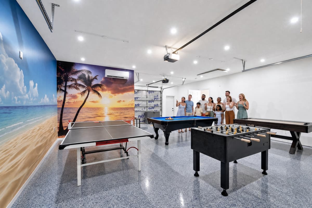 Nobody expects a room like this behind a Clearwater house. Ping-pong, foosball and a full-size pool table under a beach mural, with a projector screen at the far end. Air-conditioned, epoxy floors, room to circle every table without hitting a wall.