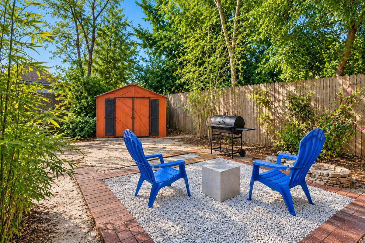 Charming outdoor lounge space with blue Adirondack chairs, a gravel patio, and lush greenery for added privacy.