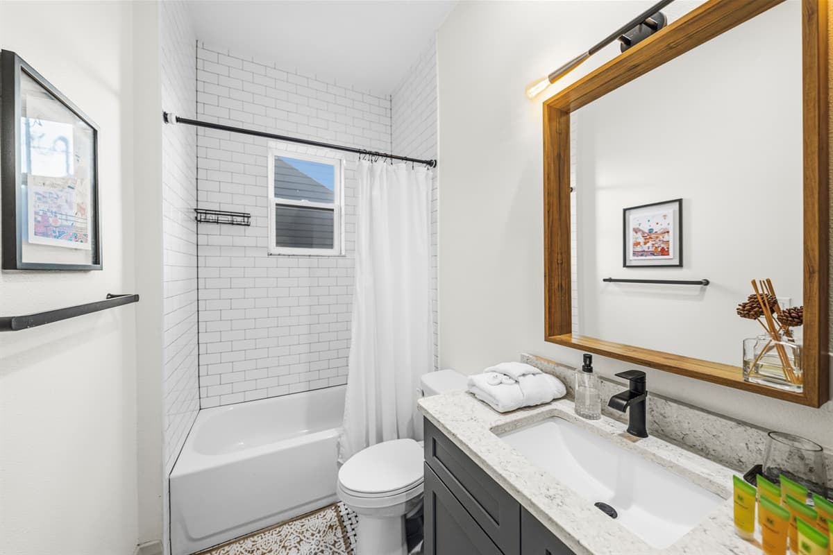 Brand-new guest bathroom with a deep soaking tub, white subway tile surround, dark wood-framed mirror, charcoal vanity with white quartz counter, and matte black fixtures. Clean, modern, and luxurious.