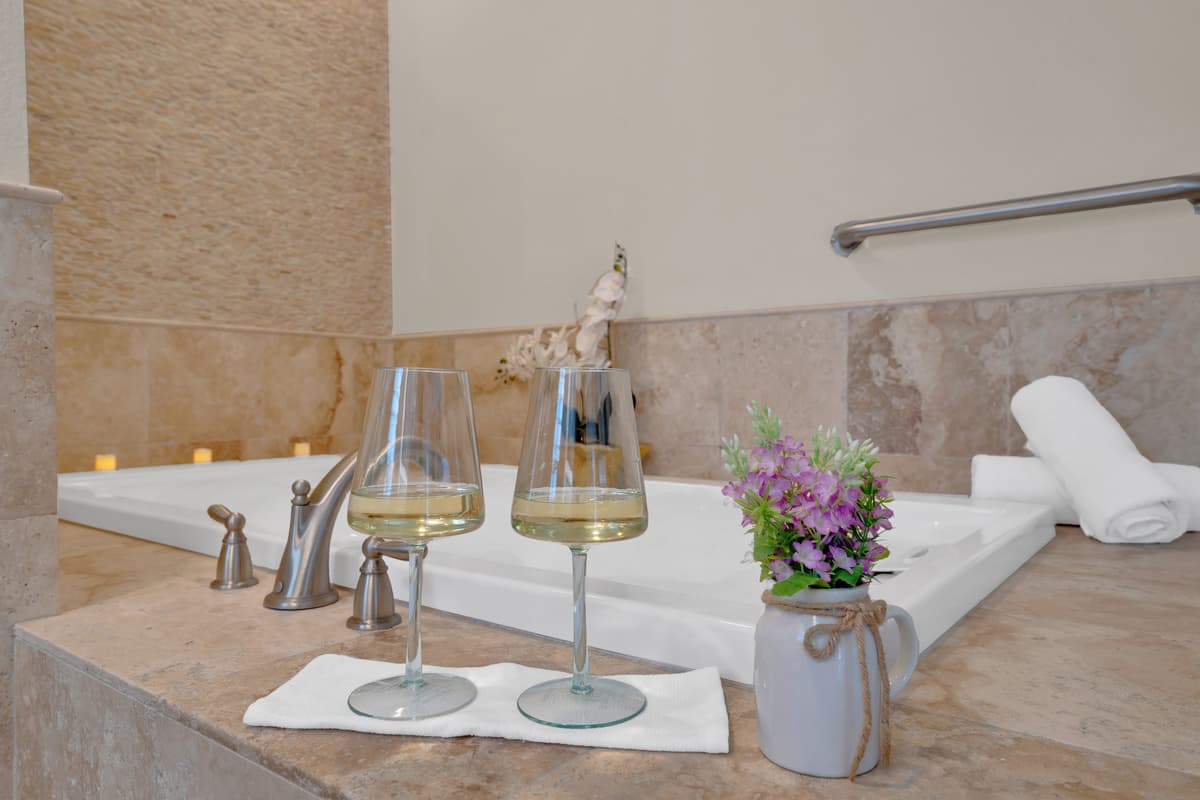 015-A soaking tub styled with wine glasses and fresh orchids turns bath time into a private spa moment inside the primary suite