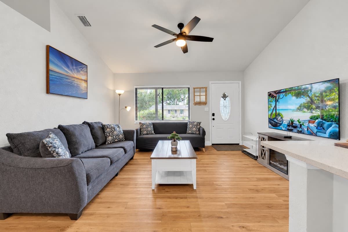 Vaulted ceiling, ceiling fan turning, two full sofas and a big Smart TV — room enough that nine people can share a movie night without anyone sitting on the floor. The kitchen counter is right behind you.