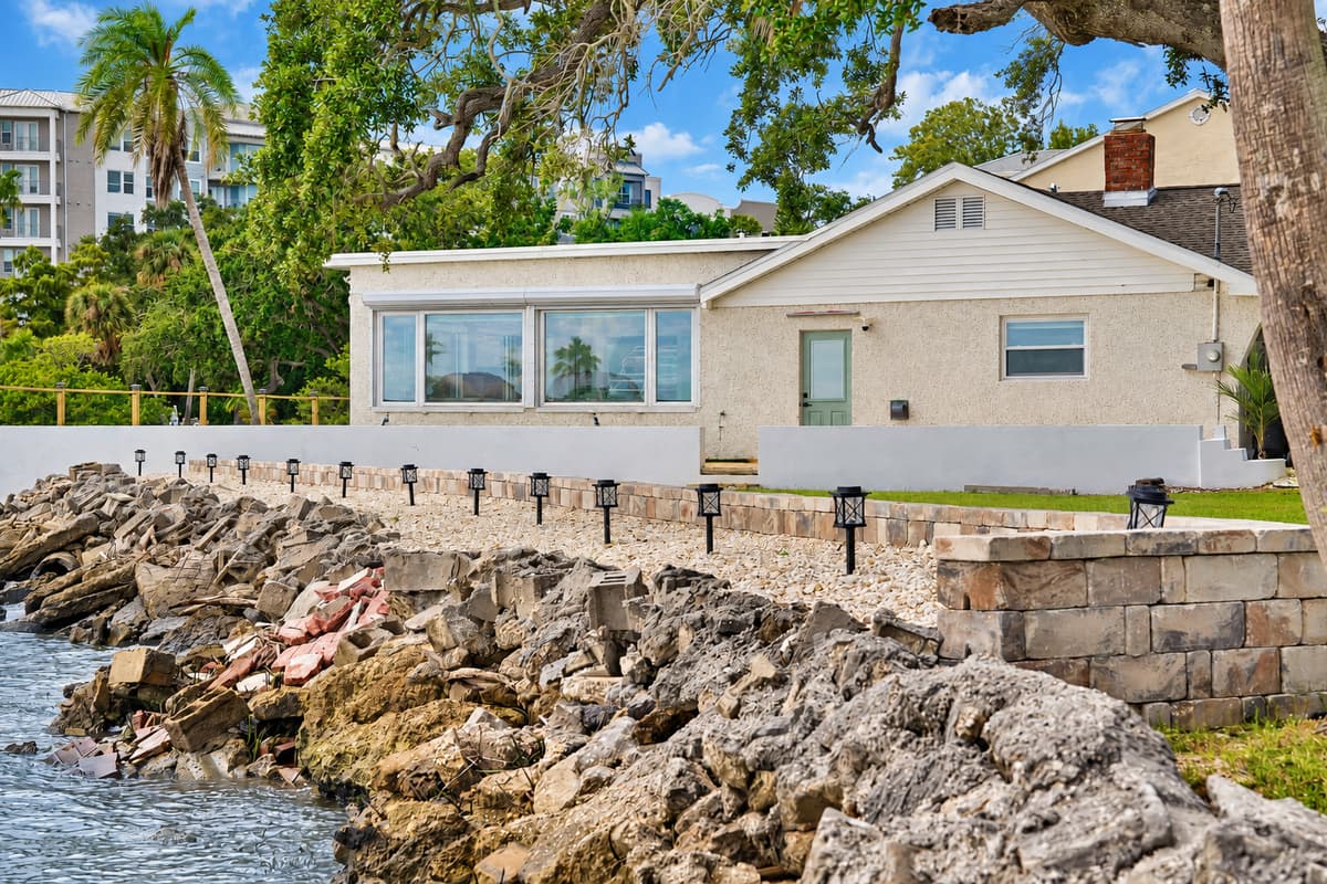 Rocky shoreline and lit seawall. The home sits right on the shoreline, with landscape lights and a stone seawall. Nature and comfort side by side.