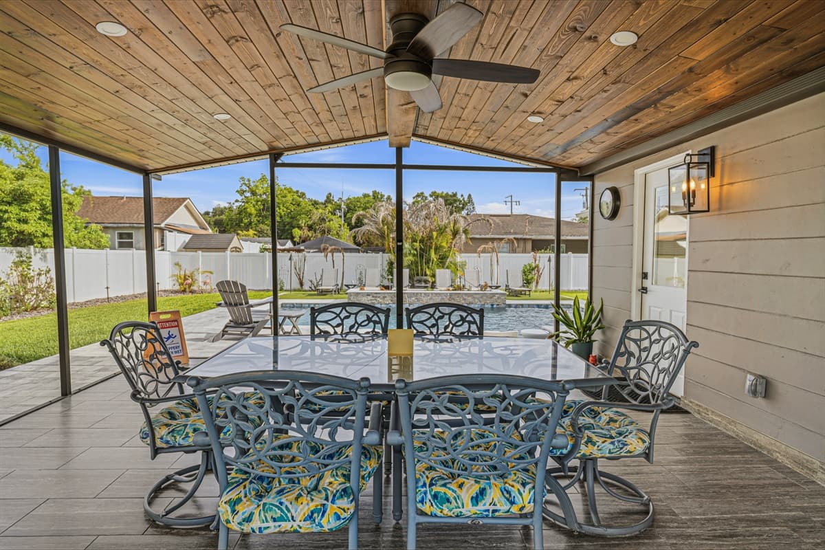 Covered outdoor dining area featuring comfortable seating, wood-paneled ceilings, and beautiful pool views.
