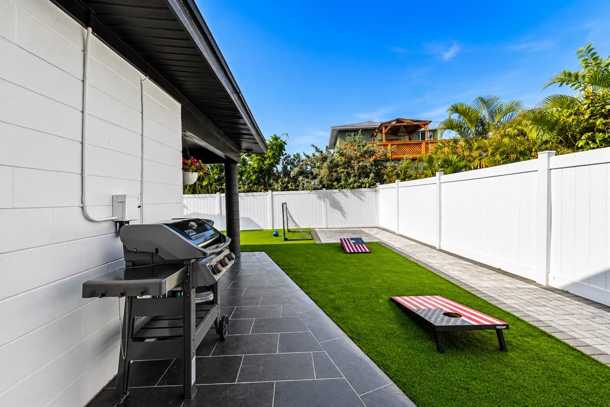 Outdoor grilling station with paved side yard and backyard lawn game setup.