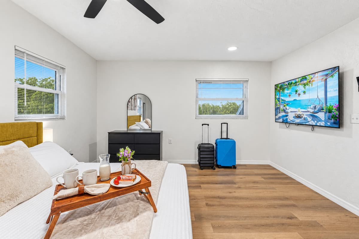Large bedroom with king bed, wall-mounted TV, and plenty of space for relaxation and comfort 
Tray and food setup shown are for staging purposes only and are not included.