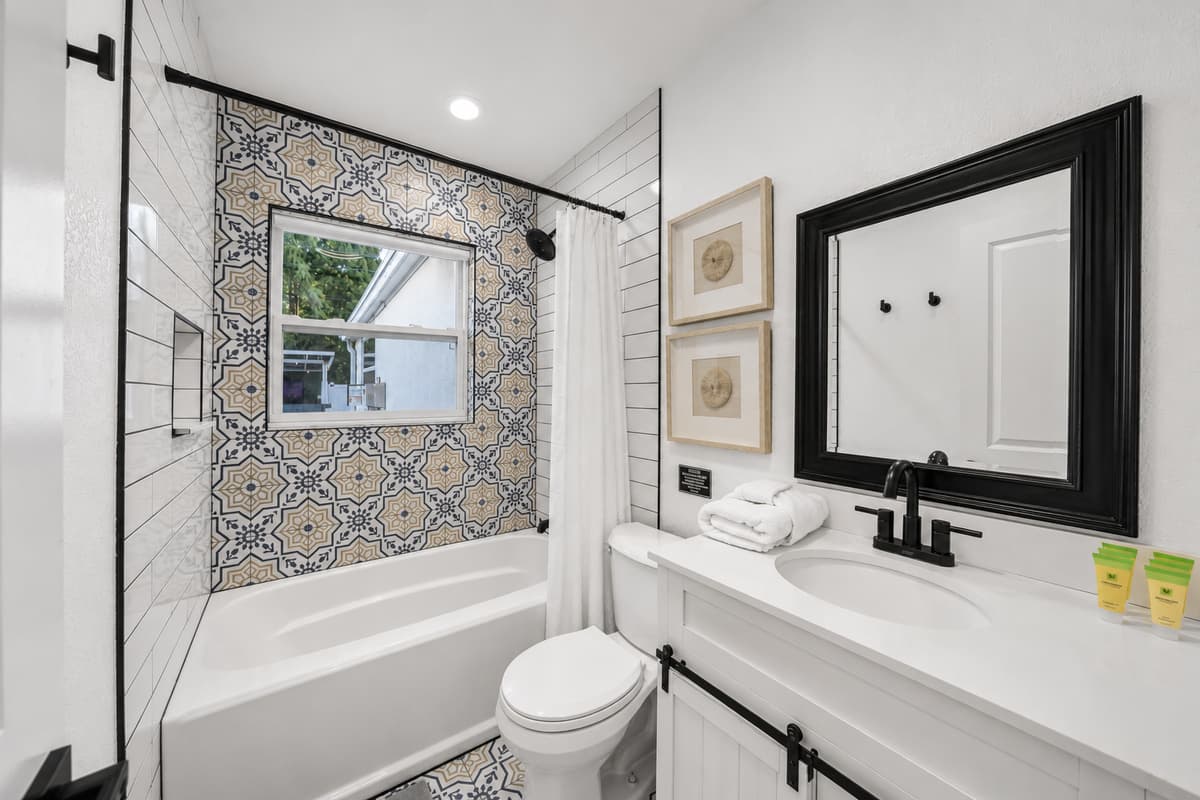 Secondary bathroom with a tub/shower combination, decorative patterned tile surround, and modern black fixtures.