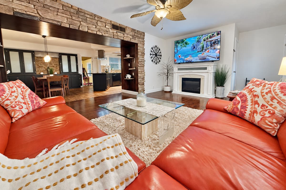 This inviting living room features a large wraparound sofa, warm wood floors, and a smart TV over a charming fireplace—perfect for movie nights or game-day lounging.