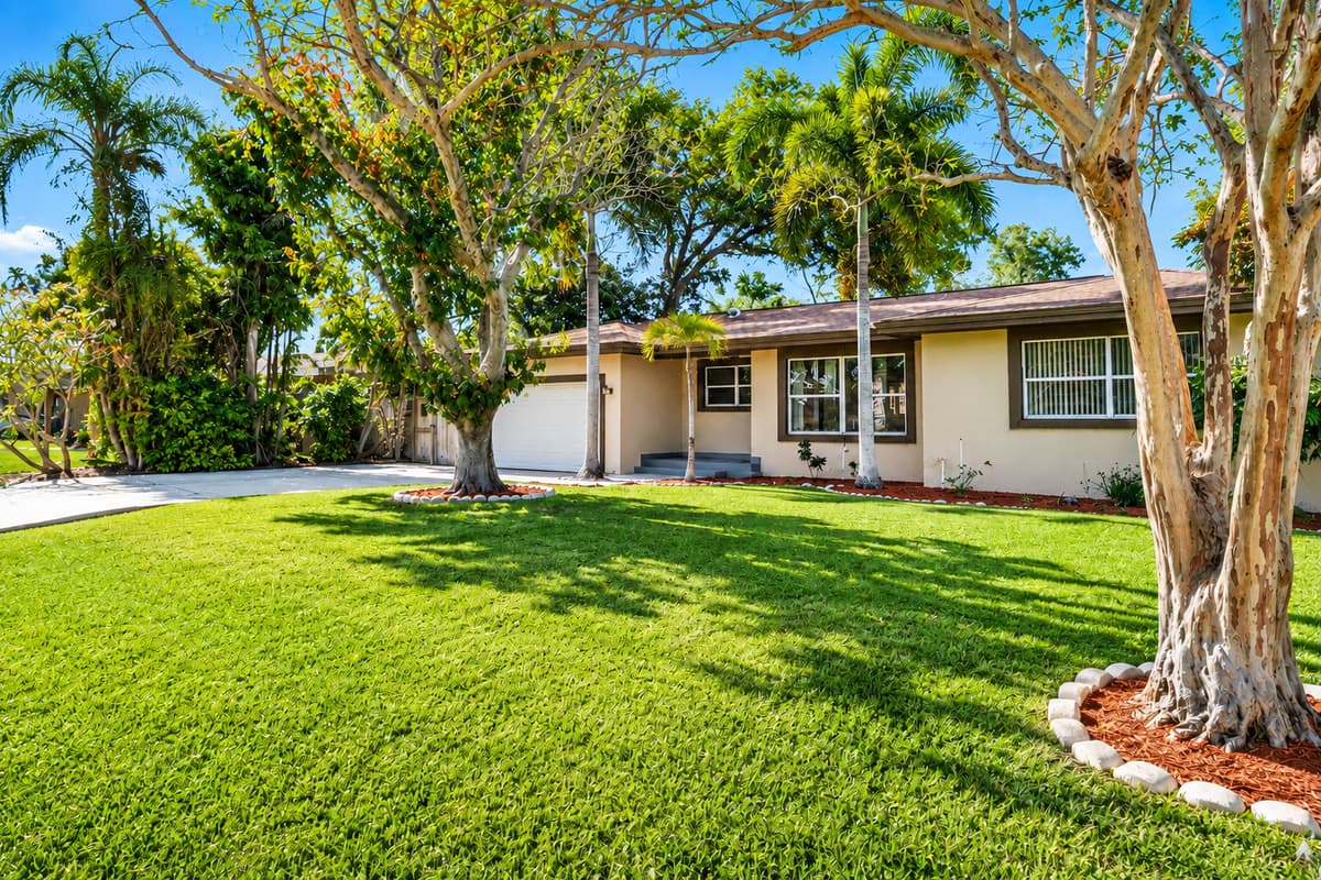 Expansive front lawn shaded by tropical trees, creating a peaceful outdoor setting.