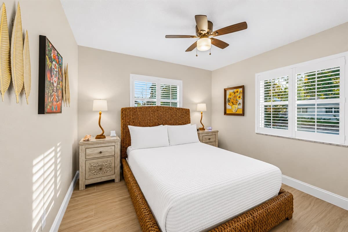 Beautifully designed queen bedroom with wicker bed frame, large windows, and charming coastal-inspired décor.