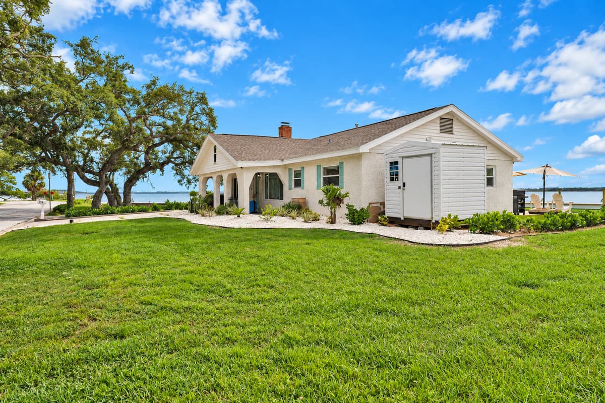 A green lawn under old oaks. The side yard opens to the bay with mature oaks and wide grass. Plenty of room for kids to run or a game of catch.