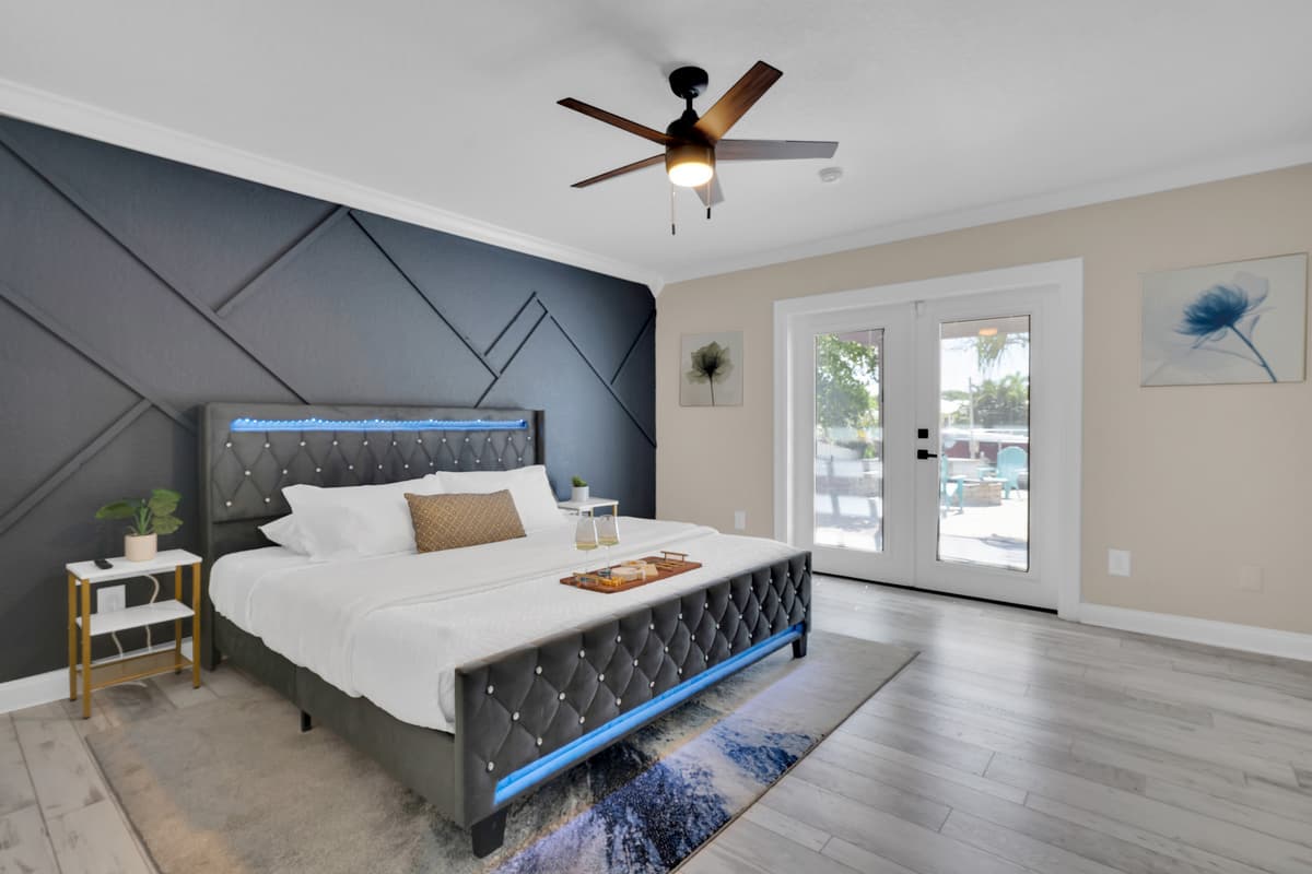008-The primary suite's tufted bed and moody accent wall open straight through French doors to the pool patio, indoor comfort meets outdoor paradise