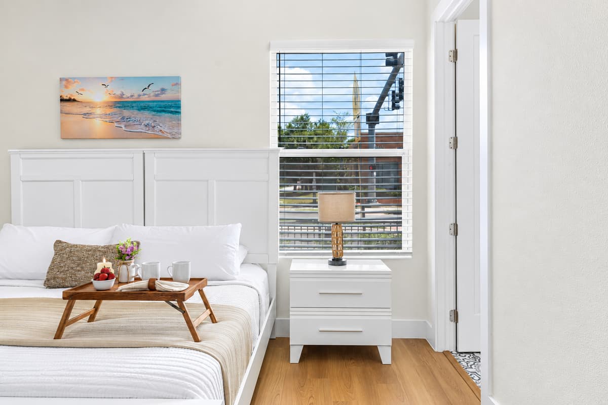 Retreat to a serene bedroom with crisp white linens, a bedside reading tray, and artwork for a hotel-like feel.