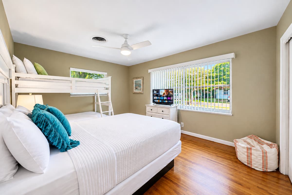 Spacious guest bedroom with comfortable sleeping arrangements, TV, and large windows overlooking the yard.