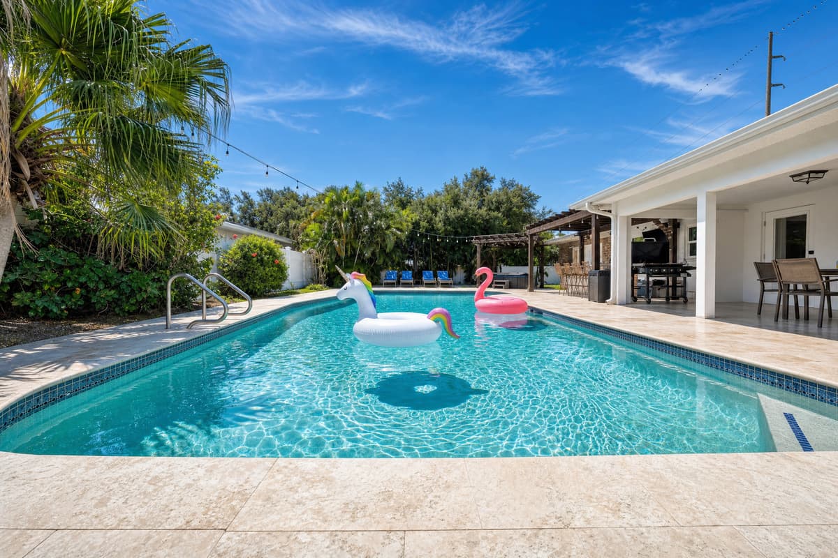 Wooden loungers lead straight to the pool where flamingo and unicorn floats bob lazily, palm trees framing a true tropical retreat.