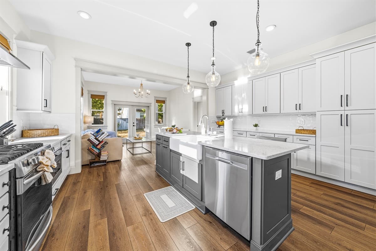 The full open-concept kitchen layout — brand-new from top to bottom with a large island, stainless appliances, pendant lighting, and a direct view through to the dining area and back patio French doors.