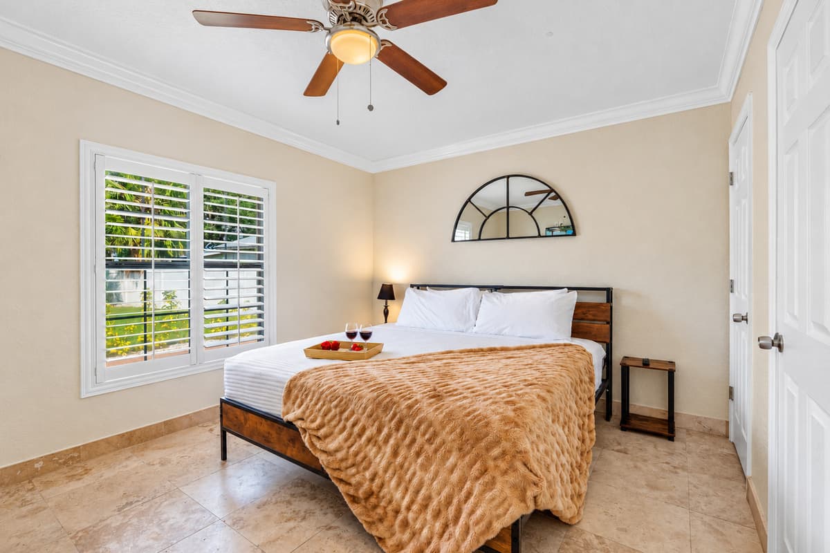 This inviting bedroom features a warm, textured throw, a rustic wood-and-metal bed frame, and plenty of natural light through plantation shutters.