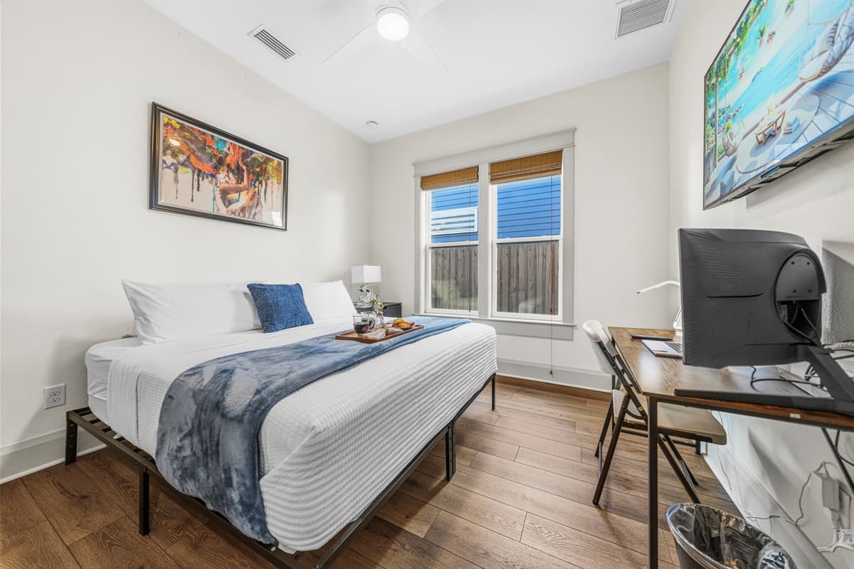 Bright & stylish bedroom in this brand-new Seminole Heights home — featuring crisp white walls, rich hardwood floors, vibrant original artwork, and large windows with bamboo shades for the perfect blend of comfort and modern flair.