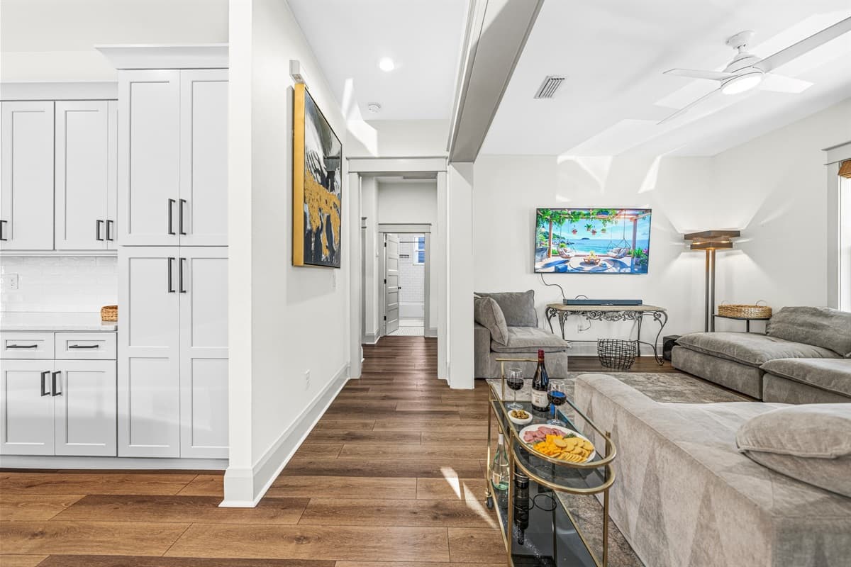 The seamless flow from kitchen to living room in this brand-new home is highlighted by tall ceilings, white shaker cabinetry, a striking piece of original artwork, and gleaming hardwood floors connecting every space.