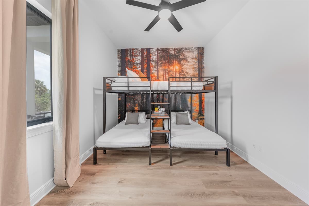 Stylish bunk room with multiple beds and a forest-themed accent wall, perfect for kids or groups.