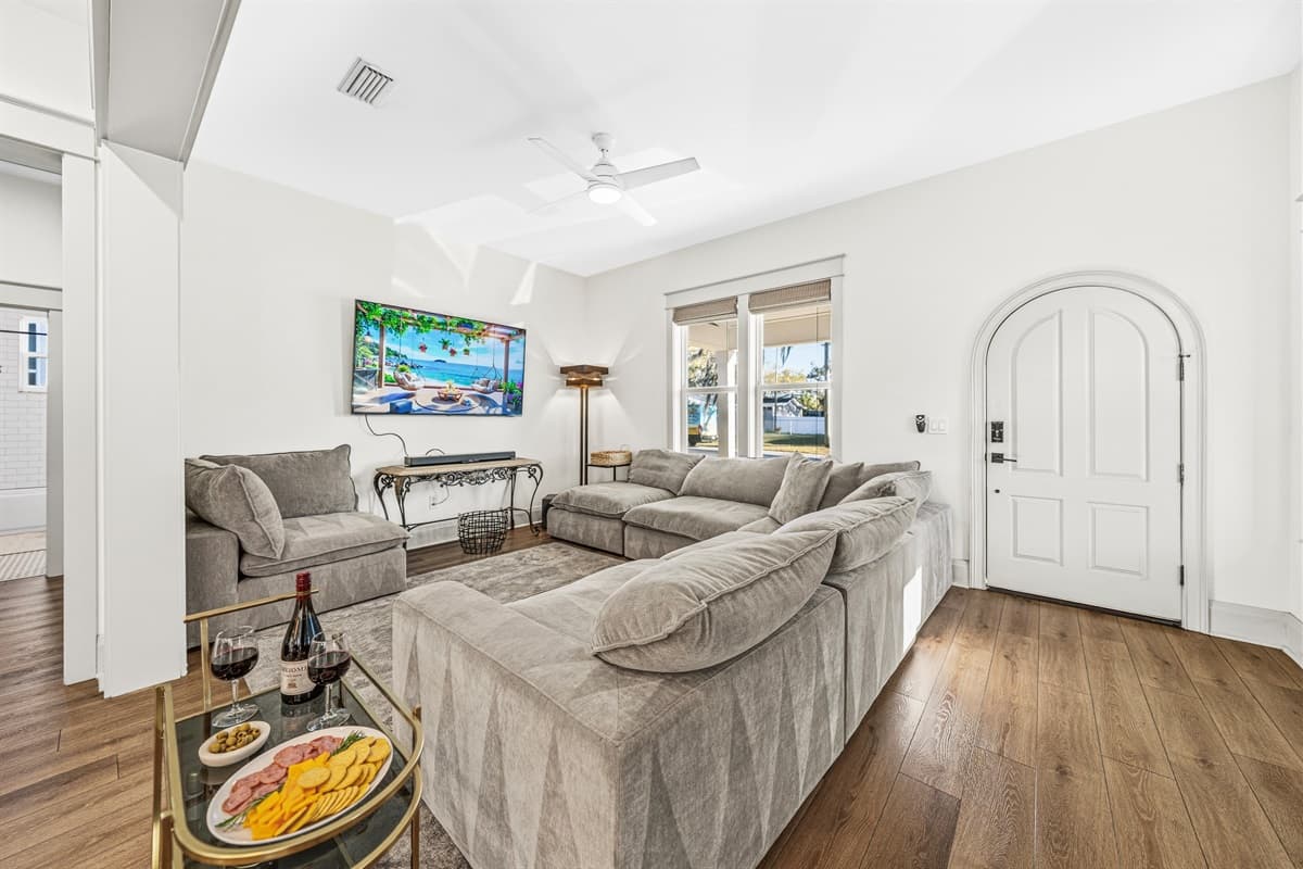 Wide-open living room with a stunning arched interior doorway, rich hardwood floors, smart TV, and a coffee table set up for entertaining. This brand-new home in Seminole Heights is built for making memories.