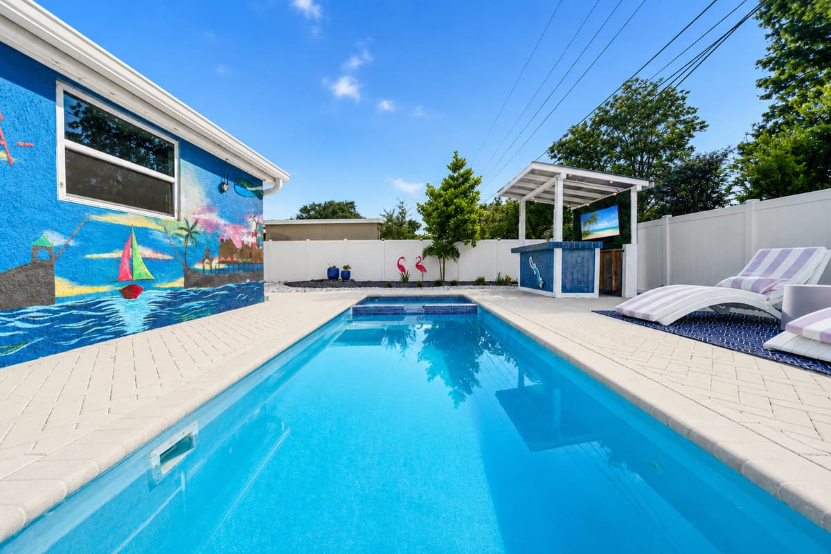 Long view of the pool area highlighting the expansive paver deck, outdoor entertainment bar, and tropical atmosphere.