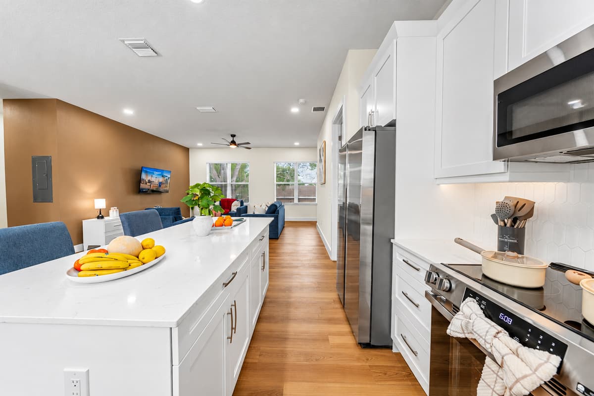 Breakfast prep with a view of the sofa. Long white island, stainless range, and a straight sightline into the living room. Flip pancakes while the kids pick the morning cartoon. Nobody disappears into a closed-off kitchen.