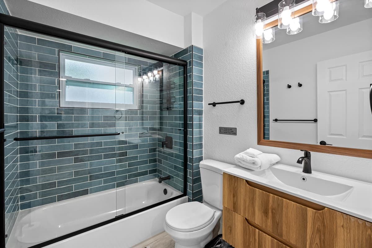 Bedroom 1 - Ensuite: Stylish and sleek, this bathroom features a stunning teal-tiled tub/shower combo, modern matte black fixtures, and a warm wood vanity for a spa-like touch.