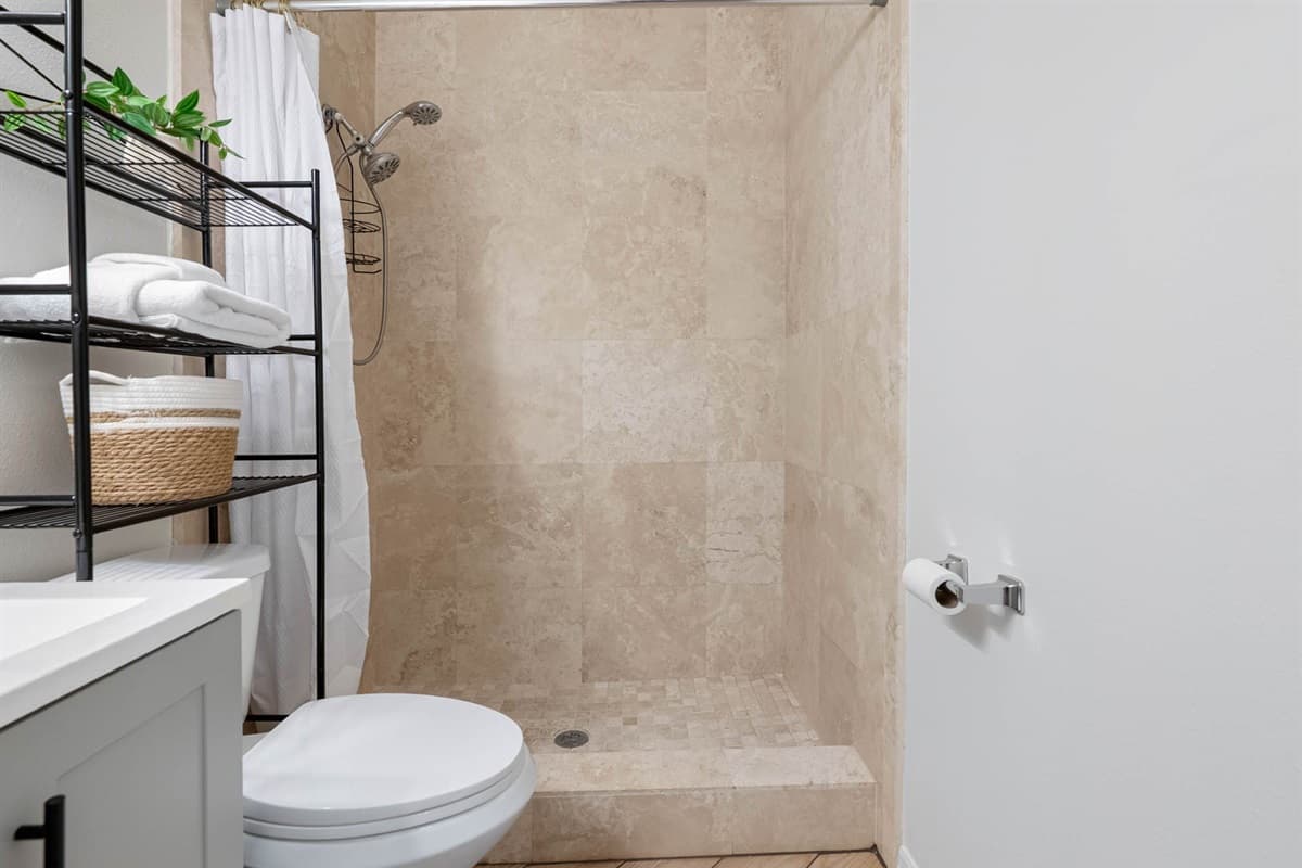 The neutral-toned stone shower pairs perfectly with the sleek vanity, while open shelves offer easy access to essentials.