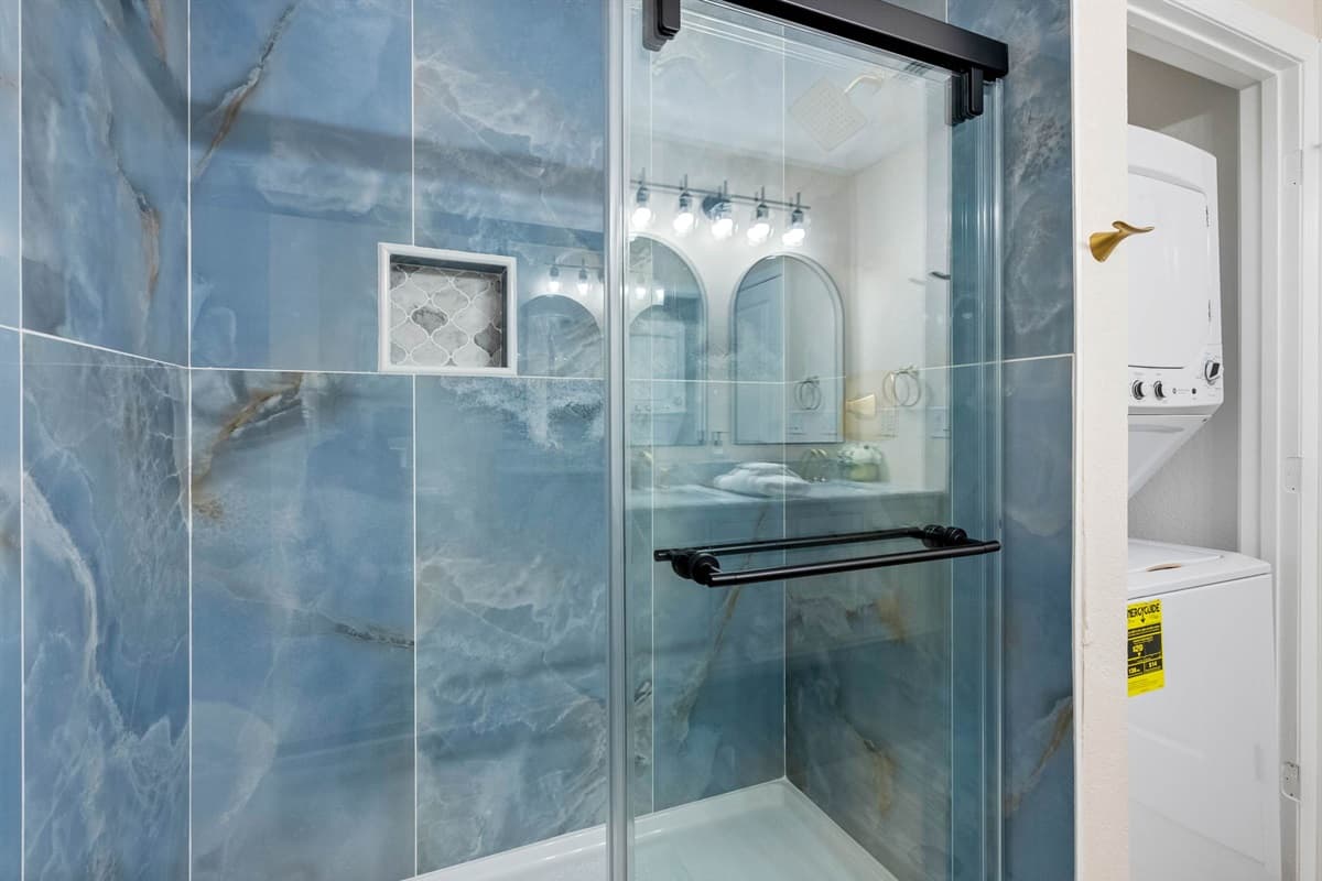 The ocean-hued shower tiles and gold accents bring a subtle coastal touch, perfect for a beachside retreat.