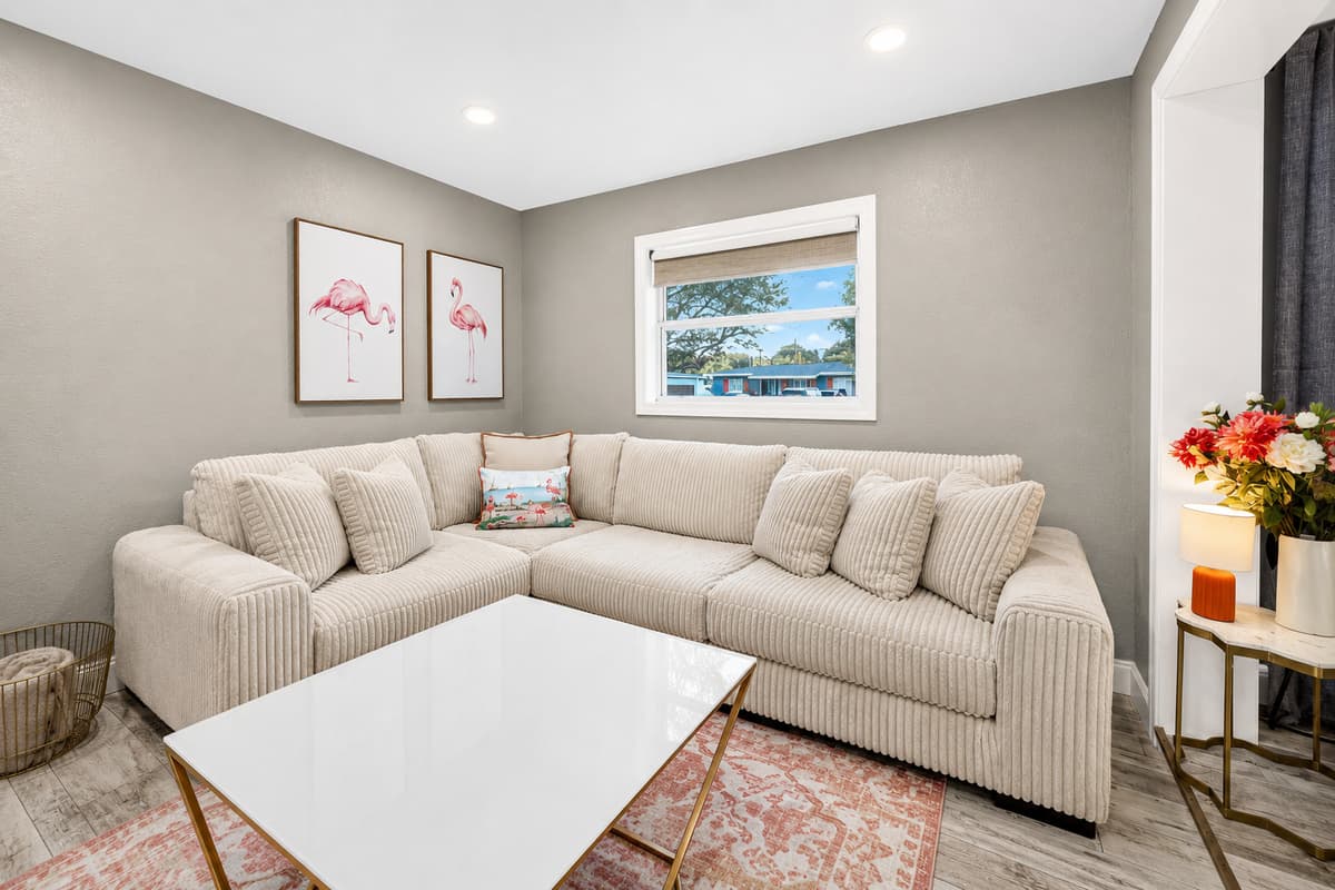 Cozy sectional sofa with plush cushions, framed flamingo artwork, and abundant natural light.