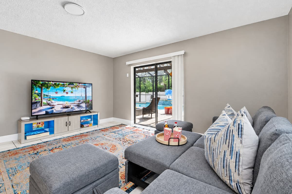 The centerpiece of the room is a modern gray sectional couch, plush and roomy, complete with a pair of matching ottomans for extra legroom or casual seating.