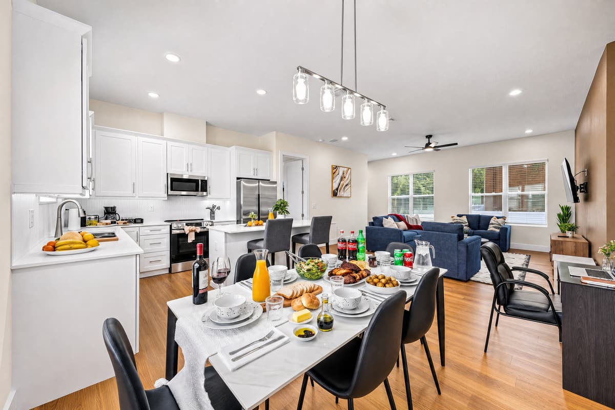 Full kitchen, island with bar seating, six-seat dining table, and sofas beyond. Room for everyone at once.