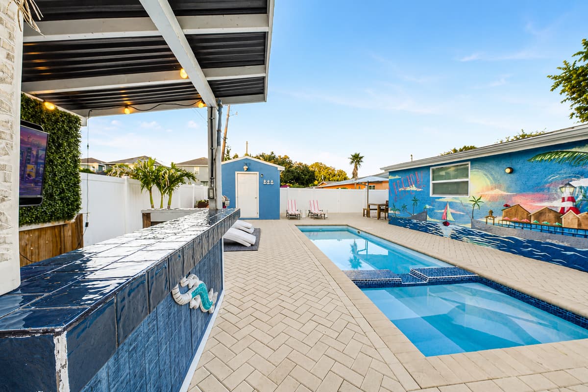 Covered outdoor entertainment bar with TV and seating, overlooking the pool and backyard gathering spaces.