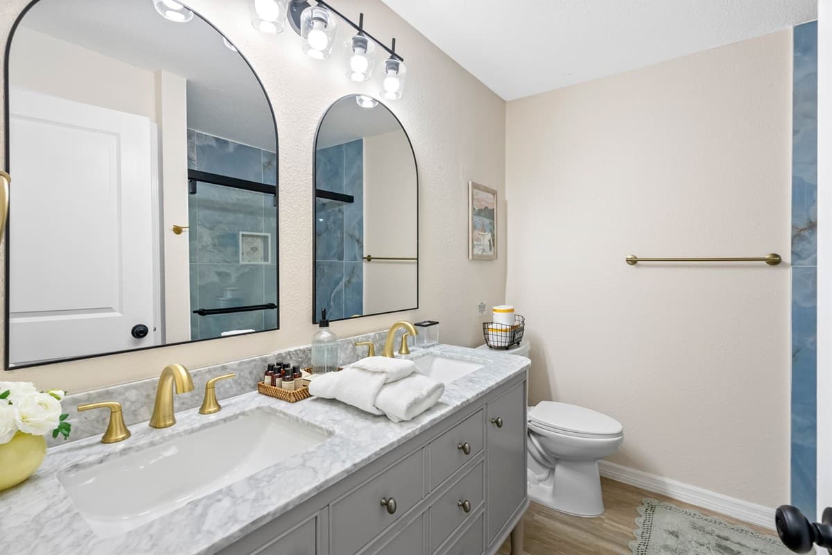 This bathroom features stunning blue-gray tile in the walk-in shower paired with brushed gold fixtures, creating a tranquil, high-end look.