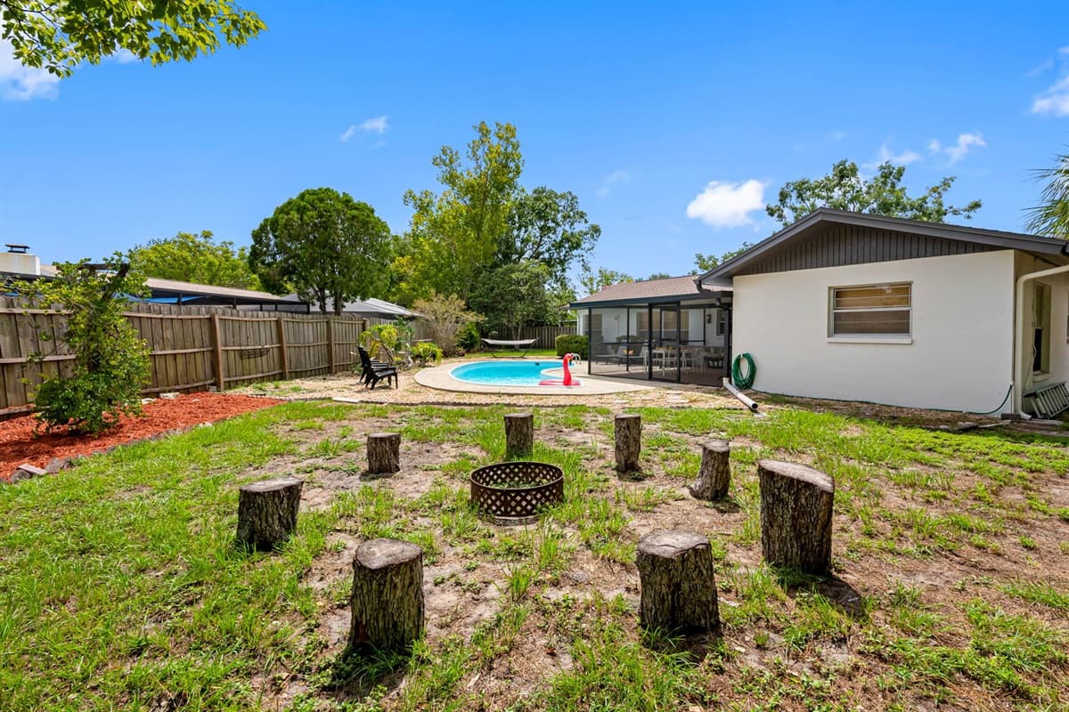 Step into your private outdoor oasis featuring a sparkling pool, cozy fire pit with log stump seating, and a relaxing hammock tucked under blooming trees—perfect for unwinding after a day of Tampa adventures.