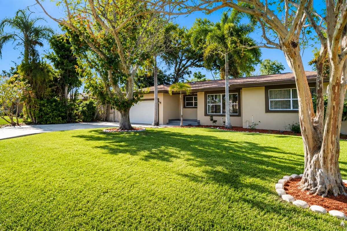 Expansive front lawn shaded by tropical trees, creating a peaceful outdoor setting.
