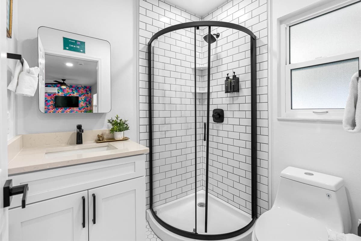 Features a spacious walk-in shower with a rainfall showerhead, enclosed in clear glass to maintain the bathroom's open and modern feel.