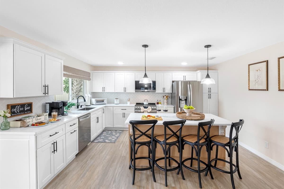 This spacious kitchen features crisp white cabinetry, sleek countertops, and a large island with seating for four — perfect for casual meals and conversation.
