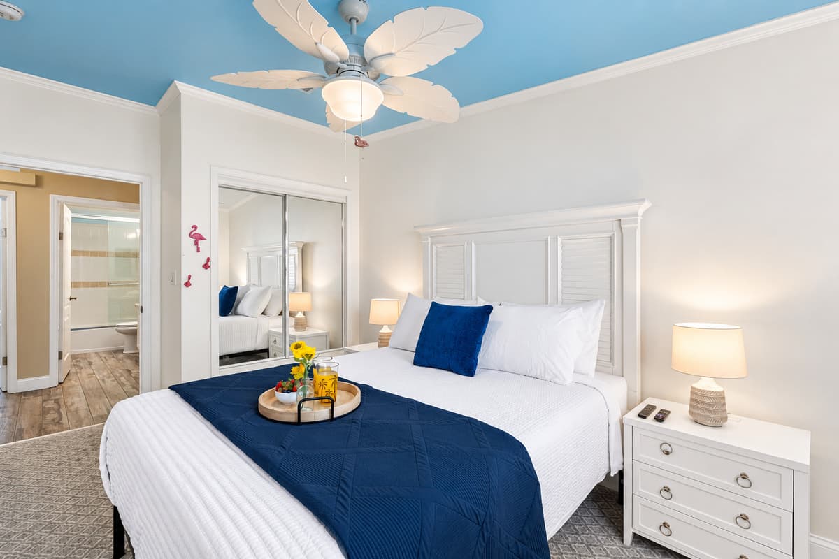 This bright and inviting bedroom features a queen bed with crisp white linens and a calming navy accent blanket.