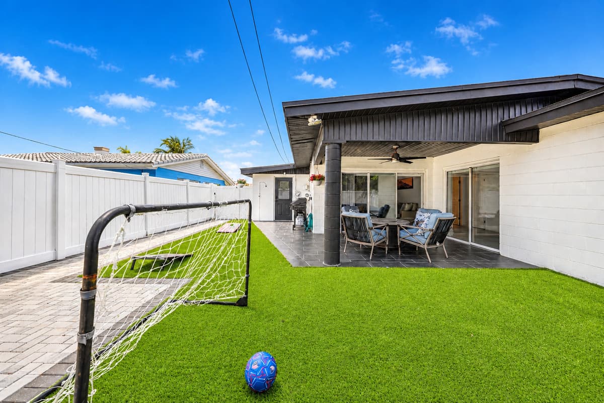 Bright and open backyard area with artificial grass, soccer goal, and patio access.
