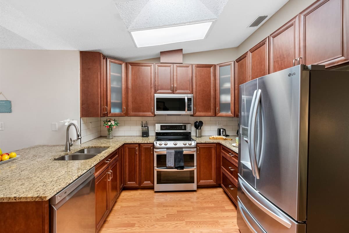 The space includes a full-size refrigerator, oven, stove, microwave, dishwasher, and a coffee maker, as well as essentials like pots, pans, baking sheets, knives, cutting boards, and a variety of cooking tools.