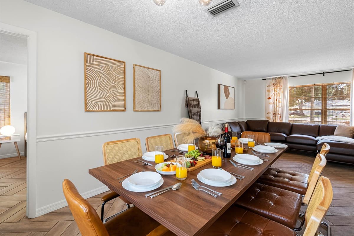 This chic dining area features a modern wood table, woven-back chairs, and plenty of natural light pouring in through soft linen curtains.