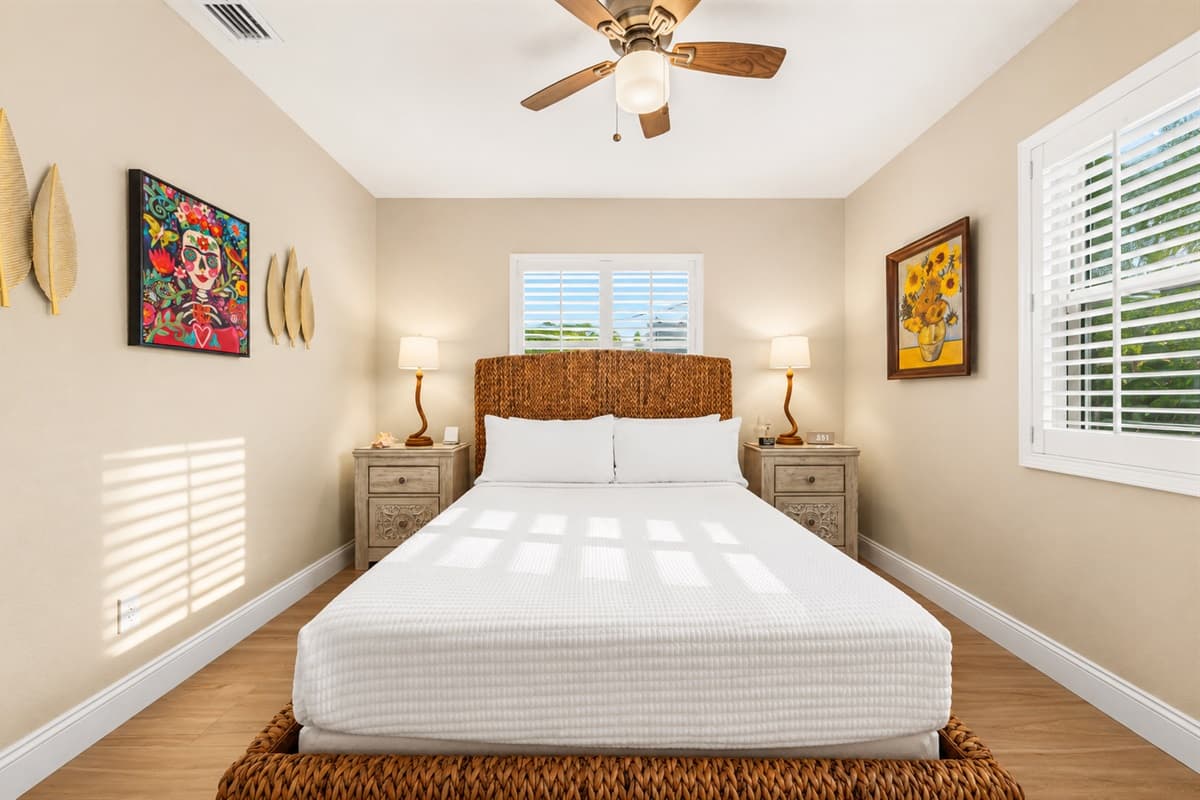 Bright and airy bedroom featuring a queen-size bed, colorful artwork, and abundant natural light.