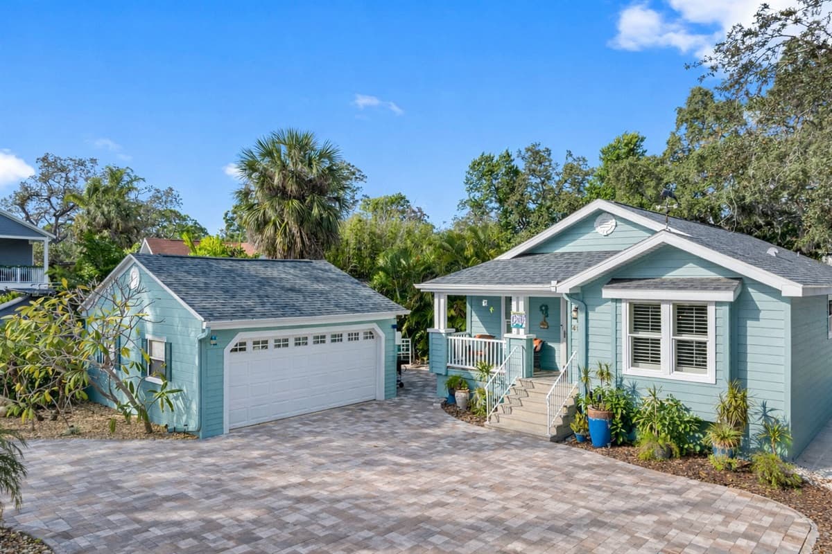 A picture-perfect cottage with a large paver courtyard, manicured gardens, and a pastel-painted façade.